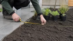 Tuinier meet de plantlijn vanaf de rand van een stenen terras
